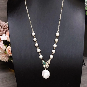 Elegant baroque pearl necklace with golden butterfly clasp and green inlay on a black stand
