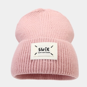 Detail of light pink knitted beanie featuring a textured weave and a white logo patch