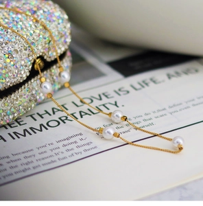 Detailed shot of a gold chain necklace with five white pearls on a stylish magazine