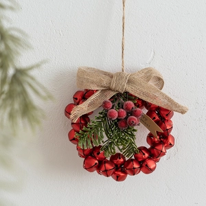 Christmas bell wreath with red berries, pine needles and burlap bow on white wall