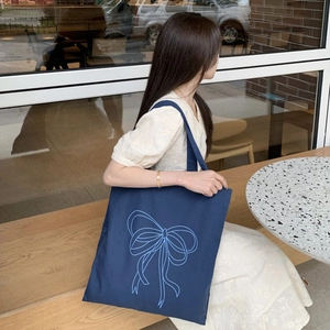 Detail einer dunkelblauen Canvas-Tasche mit blauem Schleifendruck, getragen in einem Café