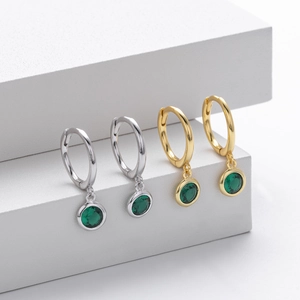 Detail of silver and gold hoop earrings featuring elegant round green gemstone pendants