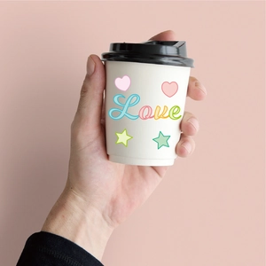 Close-up of hand holding a white disposable coffee cup with Love and heart motifs