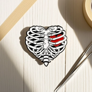 Macro shot of skull rib cage enamel pin with a red heart on a light wood surface