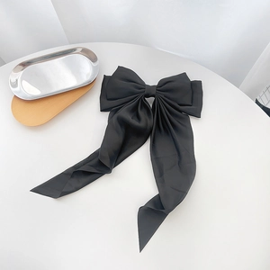 Close-up of a large black satin bow hair clip with elegant long flowing ribbons on a white surface