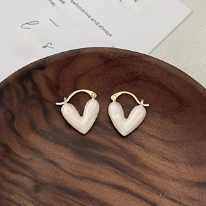 Elegant gold heart earrings with white marble enamel finish on a dark wooden base