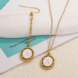 Detail of gold oval pendant with white enamel letter A and vintage wavy edge border