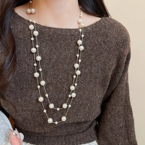 Detail of layered pearl necklace over dark sweater showing crystal bead accents