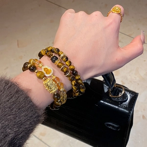Detail of tiger eye and crystal beaded bracelets with golden charms on hand