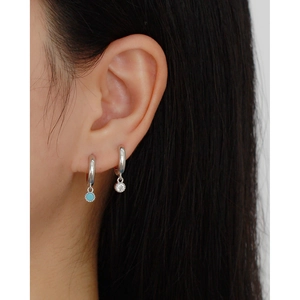 Detail of silver S925 huggie hoop earrings with blue stone and white zircon pendants