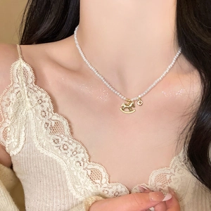 Close-up of pearl necklace featuring a golden horse pendant and zircon charm on a model