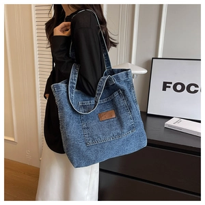 Close-up of washed denim tote bag featuring a leather logo patch and large front pocket