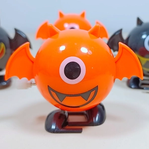 Close-up of orange wind-up bat toy showing large eye and mechanical walking mechanism