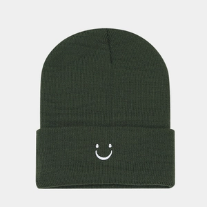 Dettaglio del ricamo bianco con faccina sorridente su un berretto in maglia verde scuro