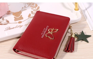 Detail of red fold wallet with gold butterfly charm and tassel on wood surface
