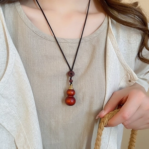 Detail of wooden gourd pendant with gold accents on a black woven necklace cord