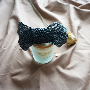 Close-up of black woven leather bow hair clip on a vintage decorative candle jar