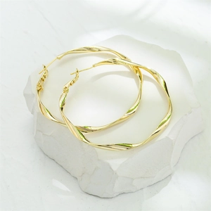 Polished golden twisted hoop earrings displayed on a white stone background