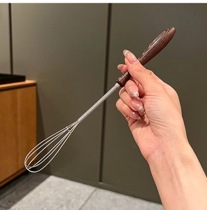 Close-up of wooden handle whisk being held, highlighting its durable stainless steel head