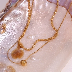 Close-up of dual-layer gold beaded necklace with hammered ball pendant in shell