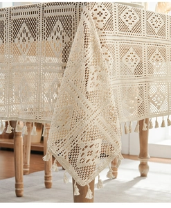 Macro detail of beige crochet lace tablecloth with geometric cutouts and fringe tassels