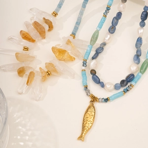 Natural stone necklace with blue crystals, pearls and a golden fish pendant on white