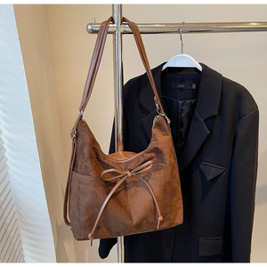 Close-up of brown suede shoulder bag featuring a decorative bow and retro zipper detail