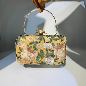 Detail of embroidered floral evening bag with metal handle and pearl clasp decor