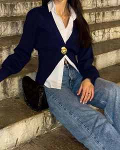 Dettaglio di un cardigan in maglia blu scuro con un singolo bottone decorativo dorato