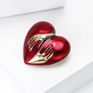 Chic red enamel heart brooch with gold hands relief on a white minimalist pedestal