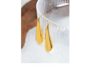 Close-up of elegant gold and cream teardrop earrings hanging on a textured glass vase