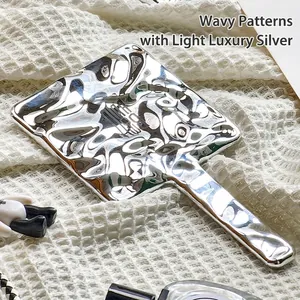 Sleek silver handheld makeup mirror with fluid wave texture and minimalist handle design