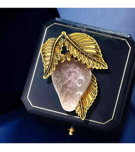 Detailed view of strawberry brooch with pink resin fruit and gold leaves on blue box
