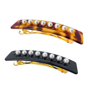 Macro detail of tortoiseshell and black acetate hair clips with white pearls set in gold