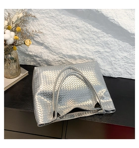 Detailed close-up of a silver woven tote bag with metallic luster on a stone background