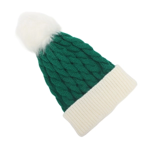 Detail of cable knit texture and white pompom on dark green winter beanie hat