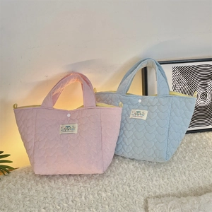 Detailed view of quilted heart pattern and snap closure on pink and blue tote bags