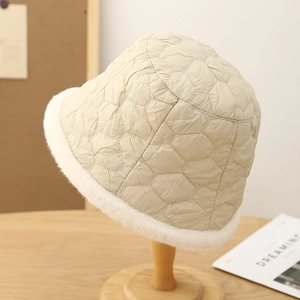 Quilted cream winter bucket hat with faux fur trim displayed on a wooden stand