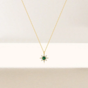 Detailed macro of golden floral pendant with green emerald center and white diamonds