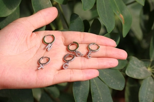 Close-up of silver zircon initial hoop earrings held in hand with several letters