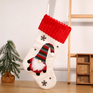 White plush Christmas stocking with red stripes and embroidered gnome on a wooden shelf