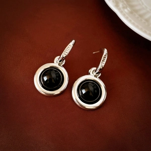 Close-up of silver geometric round earrings with black enamel center on dark background