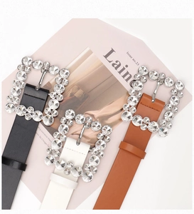 Close-up of black, white, and brown leather belts with sparkling rhinestone square buckles