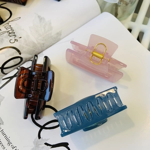 Close-up of three acrylic claw clips in pink, brown and blue on a magazine