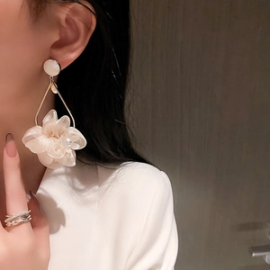 Detail of elegant beige mesh flower earring with pearls and golden metal frame on model