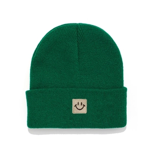 Close-up of dark green knitted beanie featuring a beige embroidered smiley face patch