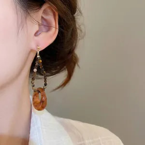 Boucles d'oreilles asymétriques en résine ambre avec finition dorée portées par mannequin