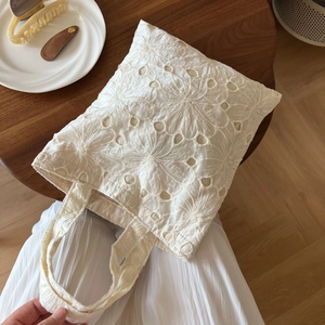 Detailed close-up of white floral lace embroidery on a vintage style cotton handbag