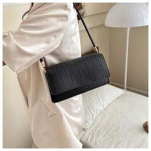 Close-up of black woven texture shoulder bag with fine metal hardware on cream silk shirt