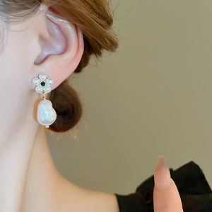 Detail view of pearl flower earrings featuring a baroque drop pearl worn on an ear